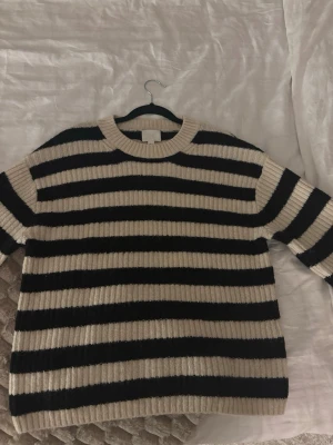 Randig stickad tröja i svart och beige - Säljer en ribbstickad tröja med breda svarta och beige ränder. Tröjan har rund halsringning och långa ärmar. Oversized passform som ger en avslappnad look. Perfekt för lager på lager och enkel att styla till jeans eller kjol.