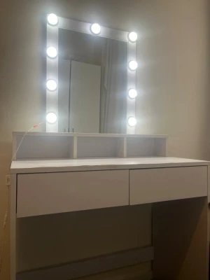 Vit sminkspegel med LED-belysning - Stilren sminkspegel med vit ram och inbyggd LED-belysning runt hela spegeln. Spegeln har en rektangulär form och står på ett vitt sminkbord med praktiska hyllor och två lådor för förvaring. Perfekt för att fixa sminket med bra ljus och ordning på dina produkter.