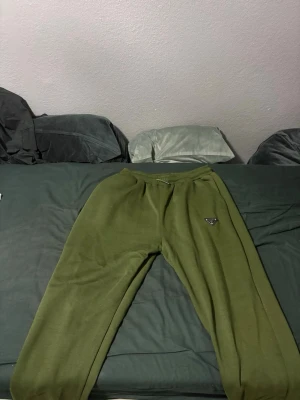 Olivgröna mjukisbyxor från Prada - Säljer ett par olivgröna mjukisbyxor från Prada med klassisk logga på vänster ben. Byxorna har elastisk midja och en bakficka. Perfekta för chill dagar eller när du vill vara extra comfy.