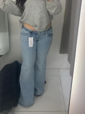 Ljusblå bootcut jeans - Säljer ett par ljusblå jeans med bootcut passform och låg midja. Jeansen har klassiska fem fickor, dragkedja och knapp framtill. Tillverkade i jeansmaterial och perfekta för en avslappnad look.