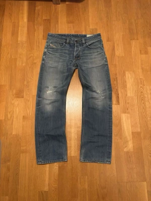 Vintage Diesel Jeans - Diesel jeans med rak passform och slitningar på låren och knäna. Jeansen har fem fickor, knappgylf och tydliga tvättade detaljer för en vintagekänsla. Tillverkade i robust bomullsdenim. Storlek 32/32. Alla hål är gjorde med mening för etestik. 