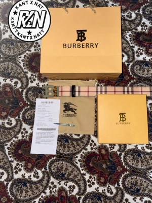  Burberry bälte - Säljer ett klassiskt Burberry-bälte i beige med det ikoniska rutmönstret och en stor guldfärgad B-spänne. Bältet är tillverkat i canvas och läder, perfekt för att lyfta vilken outfit som helst. Kommer med originalpåse och box.