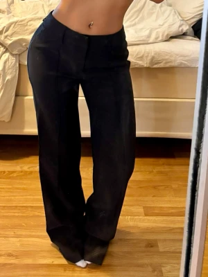 Svarta kostymbyxor med wide fit - Aldrig använda, Säljer ett par svarta kostymbyxor med hög midja och breda ben. Byxorna har klassisk look med pressveck och stängs med dold dragkedja i sidan. Materialet känns mjukt och följsamt. Stora i storleken och längden passar mer regular än short