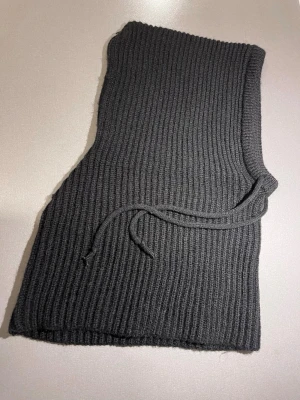 Svart stickad balaklava  - Svart stickad balaklava med ribbad struktur och snörning i kragen. Mycket varm och skön. Passar S/M. Enkel och stilren design som är lätt att matcha med olika outfits. Mycket bra skick! Säljs på flera sidor, först till kvarn. 