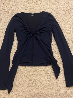 Mörkblå långärmad knyt-topp - Trendig mörkblå topp med långa ärmar och snygg knytning framtill. Djup v-ringning och croppad passform ger en modern look. Perfekt att styla med jeans eller kjol för en cool outfit. Knappt använd.
