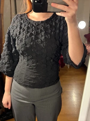 Trekvartsärmad tröja  - Säljer en svart topp med coolt strukturerat tyg och trekvartsärmar från Carin Wester. Tyvärr ett litet hål på baksidan, lätt att fixa och syns inte så mycket när tröjan är knäppt :) Storlek XS