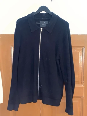 Svart kofta med dragkedja från Jack & Jones - Stilren svart kofta från Jack & Jones med hel dragkedja framtill och klassisk krage. Långärmad modell i mjukt material som passar perfekt till lager på lager under höst och vinter. Enkel och clean look som funkar till det mesta.