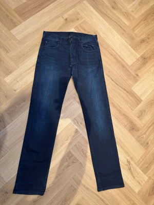Mörkblå jeans från Emporio Armani - Snygga mörkblå jeans från Emporio Armani med klassisk femficksdesign och raka ben. Jeansen är tillverkade i bomull med en liten del elastan för extra komfort. Perfekta för dig som gillar stilrena och tidlösa jeans.