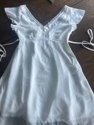 Söt klänning  - Söt vit klänning med v-ringning och spetsdetaljer vid bysten. Snöre som knyts i ryggen för en fin passform. Perfekt om man vill ha en simplare studentklänning💕