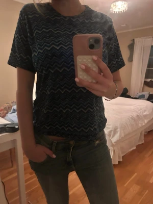Blå zigzag-mönstrad t-shirt - Säljer en blå t-shirt med coolt zigzag-mönster i olika blå toner. Super coolt mönster men får aldrig användning för de. Storlek s. Vet dock tyvärr inte vad märket är då jag köpte den på en marknad i Spanien.