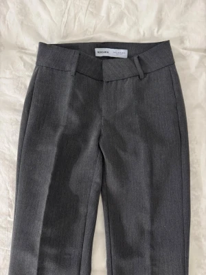 Grå kostymbyxor från Bershka - Snygga grå kostymbyxor från Bershka med bootcut passform. Byxorna har hällor för bälte och är tillverkade i ett mjukt material som känns bekvämt hela dagen. Perfekta för en stilren och modern look. Använd endast fåtal gånger, precis som ny!