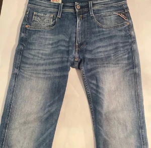 Replay Anbass jeans blå slim fit - Snygga Replay Anbass jeans i klassisk blå tvätt med coola slitningar och smal passform. Modellen har fem fickor, dragkedja och knappstängning. Jeansen är tillverkade i mjukt bomullsmaterial med stretch för extra komfort. Har inga skador och är i mycket bra skick. Vid minsta fundering kontakta mig…