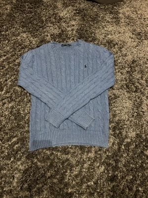 Blå kabelstickad tröja Polo Ralph Lauren - Snygg blå kabelstickad tröja från Polo Ralph Lauren i storlek S. Tröjan har rund hals, lång ärm och klassisk broderad logga på bröstet. Tillverkad i mjuk bomull som känns skön mot huden. Perfekt för dig som gillar stilrena och tidlösa plagg.                                                                                     Storlek är S.                                                                      Pris kan diskuteras!