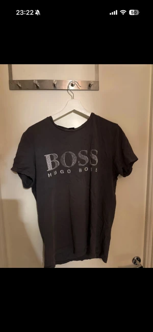 Grå t-shirt från Hugo Boss - Grå t-shirt från Hugo Boss med stort BOSS-tryck i vitt på bröstet. Klassisk rund hals och korta ärmar. Materialet är mjuk bomull och passformen är normal. (Ser bättre ut när den är strykt såklart) 