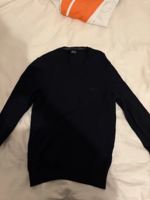 Mörkblå stickad tröja från Hugo Boss - Snygg mörkblå stickad tröja från Hugo Boss med v-ringad hals och diskret logga på bröstet. Tillverkad av finaste italienska garnet, perfekt för dig som gillar stilrena och klassiska plagg. Långa ärmar och mjuk känsla.