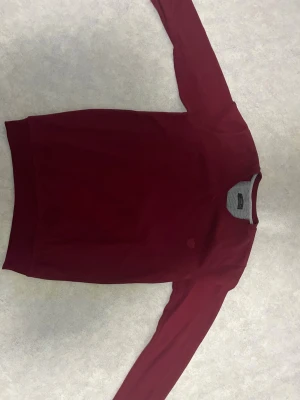 Vinröd stickad tröja från Morris - Snygg vinröd stickad tröja från Morris med broderad logga på bröstet. Tröjan har rund hals och långa ärmar, samt ribbade muddar vid hals, ärmslut och nederkant. Perfekt för dig som gillar klassisk stil med en modern touch.