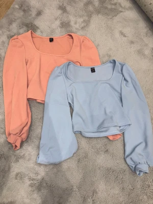 Croppade toppar i ljusblått och aprikos - Två croppade toppar, en i ljusblått och en i aprikos. Båda har lång puffärm, fyrkantig ringning och är tillverkade i mjuk polyester. Använda 1-2 gånger, st petite M, pris går att diskuteras om du är intresserad av att köpa en separat🤍