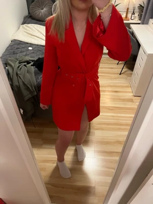 Röd omlottklänning NA-KD x Hannalicious - Snygg röd kort omlottklänning från NA-KD x Hannalicious i satinliknande material. Klänningen har lång ärm, markerad midja med bälte och djup v-ringning. Perfekt för dig som vill sticka ut med en färgstark look.