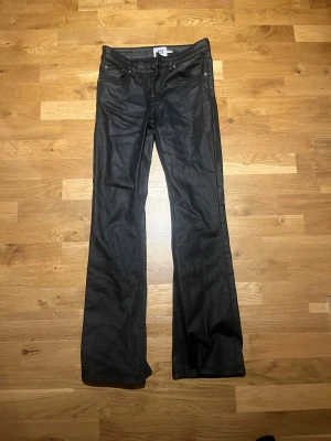 Svarta jeans - Snygga svarta byxor med bootcut passform från märket lager 157. Byxorna har klassisk femficksdesign och är tillverkade i ett material som ger en lätt glansig finish. Perfekta för dig som gillar en stilren look med lite edge.