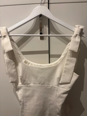 Vit topp med rosett från Zara - Supersnygg vit topp från Zara med breda axelband och rosett-detaljer på axlarna. Toppen sitter tajt och har en dragkedja på sidan🩵