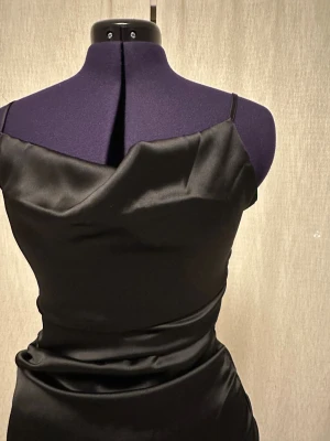 Svart satin klänning JJXX S - Svart kort klänning från JJXX i glansigt satinliknande material. Klänningen har smala axelband, draperad halsringning och figurnära passform. Perfekt för dig som gillar en stilren och elegant look.