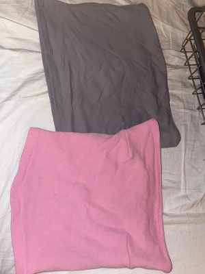 Två enkla korta bando toppar - Säljer två basic bando toppar, en i ljusrosa och en i grått. Båda har en rak och enkel design utan detaljer eller mönster, perfekta att matcha med olika kjolar. Materialet känns mjukt och stretchigt, troligen bomull eller polyesterblandning.