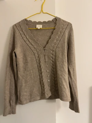 Beige kofta med detaljer - Super söt finstickad beige kofta med detaljer längst v-rigningen. Den fjärde knappen är halv, men det är inget som syns och den fungerar fortfarande som vanligt. Kolla sista bilden för färgen. Öppen för prisförslag!