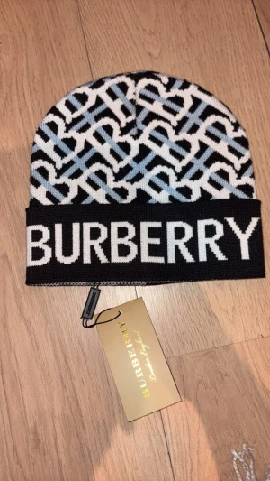 Burberry mönstrad mössa i blått och vitt - Snygg mössa från Burberry med grafiskt mönster i svart, vitt och ljusblått. Stor logotyp framtill och klassisk Burberry-tag på insidan. Stickad i mjukt material som håller dig varm och ger en cool vibe till din outfit.