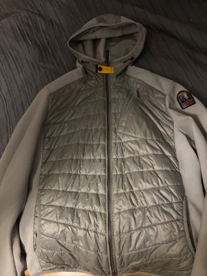 Grå quiltad pufferjacka Parajumpers - Snygg grå pufferjacka från Parajumpers med quiltad framsida, huva och coolt gult spänne vid halsen. Jackan har dragkedja hela vägen, bröstficka med zip och patch på ärmen. Perfekt för dig som gillar streetwear och vill ha något som sticker ut. Skriv DM om mer bilder och frågor även pris!!!