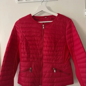 Röd quiltad pufferjacka med dragkedja - Snygg röd pufferjacka med quiltad design och rund hals. Jackan har två snedställda fickor med dragkedja och en hel dragkedja framtill. Långärmad och tillverkad i syntetmaterial, perfekt för dig som gillar färg och stil.