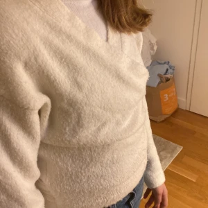 Vit omlottkofta med knyt i midjan - Mysig vit omlottkofta med knytband i midjan och lång ärm. Koftan är tillverkad i ett mjukt stickat material som känns skönt mot huden. Perfekt att slänga på sig när det är lite kyligt ute. Snygg och enkel att matcha med jeans eller kjol.