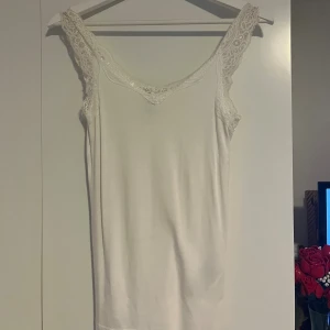Vit linnetopp med spets från Pieces - Säljer en vit linnetopp från i storlek S. Toppen har breda axelband med snygga spetsdetaljer och en mjuk, slät yta. Passformen är normal men åt det tightare hållet, formar kroppen fint 💗säljer då den inte kommer till användning längre 