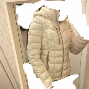  Calvin Klein vinterjacka  - Snygg vit vinterjacka från Calvin Klein med silver design, huva och dragkedjor. Jackan har lång ärm, två fickor med dragkedja och en clean look. Perfekt för kyliga dagar och riktigt skön att bära. Fluffig luva och runt kragen. Fickor på insidan också. One of a kind. Passar xxs-ungefär s