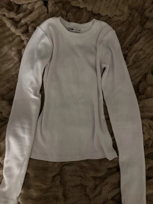 Vit ribbad långärmad tröja från Sister - Säljer en vit långärmad tröja från Sister i storlek XS. Tröjan är ribbad och har en rund halsringning, perfekt för dig som gillar enkel och clean stil. Materialet är mjukt och stretchigt, vilket gör den skön att bära hela dagen.