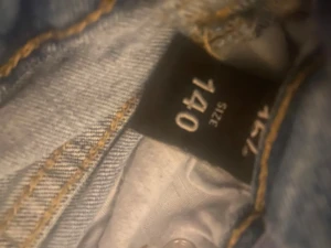 Blå denimshorts från 157, storlek 140 - Säljer ett par klassiska blå jeansshorts från 157 i storlek 140. De har fem fickor, slitna detaljer och råa kanter vid bensluten för en chill vibe. Materialet är robust denim med knapp och dragkedja framtill. Perfekt för dig som gillar streetstyle.