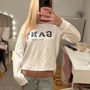 Vit långärmad GANT sweatshirt - Vit sweatshirt från GANT med mörkblå tryckt logga och text 'Est. 1949' på bröstet. Tröjan har rund hals, långa ärmar och ribbade muddar vid ärmslut och nederkant. Tillverkad i mjuk bomull, perfekt för chill dagar.