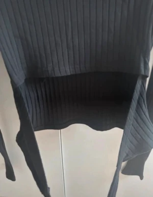 Svart ribbad tröja med öppning i ryggen - Svart långärmad topp från NA-KD med ribbad struktur och öppning i ryggen med knyt. Toppen har en croppad passform och rund halsringning. Perfekt för dig som gillar stilrena och trendiga plagg med snygga detaljer