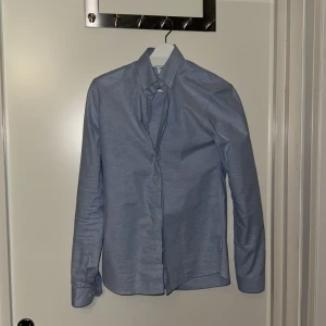 Blå slim fit skjorta Lindbergh XS - Snygg ljusblå skjorta från Lindbergh i slim fit-modell, storlek XS. Skjortan har klassisk krage med knappar och är tillverkad i mjuk bomull med Superflex för extra rörelsefrihet. Långärmad och stilren design, perfekt för dig som gillar en clean look.