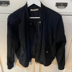 Svart bomberjacka från Gina Tricot - Svart bomberjacka från Gina Tricot. Jackan har två fickor med tryckknappar och en dragkedja framtill. Perfekt enkel jacka som passar till allt!