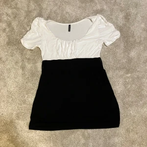Svartvit topp från Amisu - Supersöt svartvit topp från Amisu i storlek XS. Den har kort ärm med lätt puff, midja där det finns möjlighet att knyta band runt (inget band ingår). Överdelen är vit och nederdelen svart, vilket ger en snygg kontrast. 