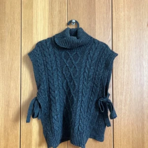 Mörkgrå stickad väst med polokrage - Snygg mörkgrå stickad väst från Mamalicious i storlek XS. Den har polokrage, grova kabelstickade detaljer och knytband på sidorna. Säljer pågrund av att den inte kommer till användning längre. Bara att höra av sig vid frågor// Amanda❤️