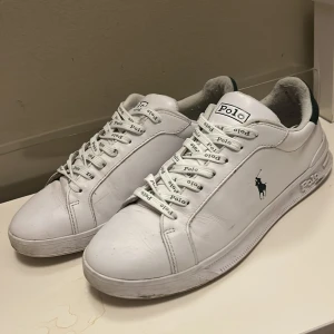Vita Polo Ralph Lauren sneakers -  Priset kan diskuterat. Använda få antal gånger. Kan gå med på byten.Fräscha vita sneakers från Polo Ralph Lauren med gröna detaljer på hälen och klassisk logga på sidan. Skorna har snörning med Polo-tryck på skosnörena och är tillverkade i skinn för en clean och stilren look. Perfekta för dig som gillar tidlös och sportig stil.