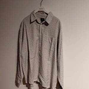 Rutig loose fit skjorta från H&M - Säljer en vit och grå rutig skjorta från H&M i loose fit. Skjortan har klassisk krage, lång ärm och knappar framtill. Perfekt för dig som gillar streetwear eller bara vill ha en finare skjorta.. Materialet är mjukt och känns skönt mot huden.