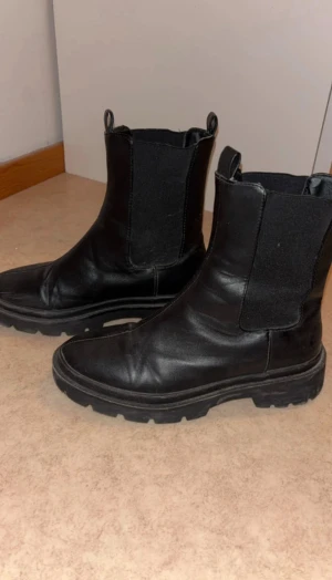 Svarta chunky chelsea boots - Säljer ett par svarta chelsea boots med rund tå. Bootsens är i skinn material och har elastiska paneler på sidorna för enkel på- och avtagning. Perfekt för dig som gillar en stilren och edgy look. (Kommer självklart torka av dom noggrant innan jag skickar iväg dom )