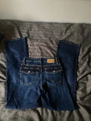 Bootcut jeans från 157, mörkblå - Mörkblå bootcut jeans från 157 med klassisk femficksdesign och kontrastsömmar. Modellen heter '90's Boot' och har en rak passform över låren med lätt utsvängda ben. Jeansen är tillverkade i slitstarkt denim och har snygga detaljer som metallknappar och nitar. Helt nya (xs FULL)