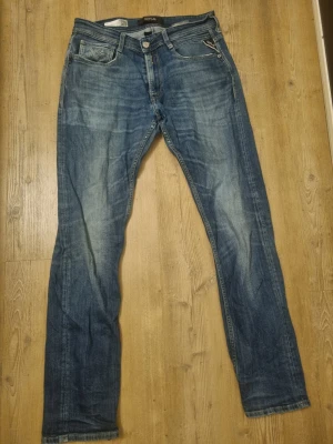 Replay Rocco jeans blå storlek 30 - Snygga Replay Rocco jeans i klassisk blå tvätt med slitningar och raka ben. Modellen har fem fickor, knappgylf och coola detaljer vid fickorna. Jeansen är tillverkade i robust denim och har en normal passform som sitter skönt hela dagen.