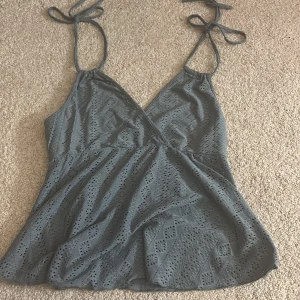 En fin topp  - Säljer en topp med omlott-design och knyt i nacken. Toppen är ärmlös och har ett snyggt hålmönster med geometriska former. Säljer den för jag aldrig använt den och kommer ej göra 