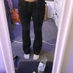 True Religion Joey Low Rise Flare jeans - Svarta jeans från True Religion, modell Joey Low Rise Flare. Snygg låg midja och utsvängda ben. Säljer dom för dom är för stora dom är också uppsydda och jag är 1,56-1,58 sen kan man ju sprätta upp dom, inte använd jätte mycket dom har en liten fläck på knät som inte går bort men det är inget man märker av
