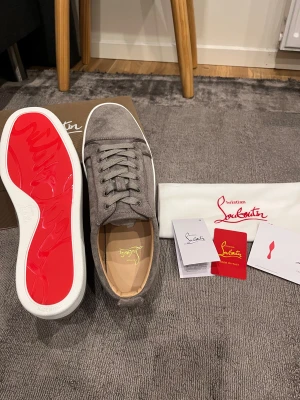 Christian Louboutin Gråa Storlek 45 - Snygga grå sneakers från Christian Louboutin i mjuk mocka med klassisk rund tå och platt vit sula. Skorna har snörning och den ikoniska röda undersulan. Insidan är beige och detaljerna är stilrena, perfekt för dig som gillar exklusiv design.