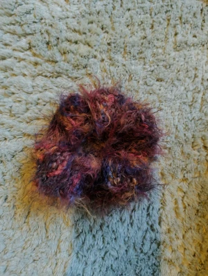 Färgglad fluffig scrunchie - En unik och fluffig scrunchie i lila, rosa och blå toner. Den är virkad med ett garn som ger ett mjukt och busigt utseende, perfekt för att ge din frisyr extra attityd. Passar dig som gillar färg och vill sticka ut med din håraccessoar.